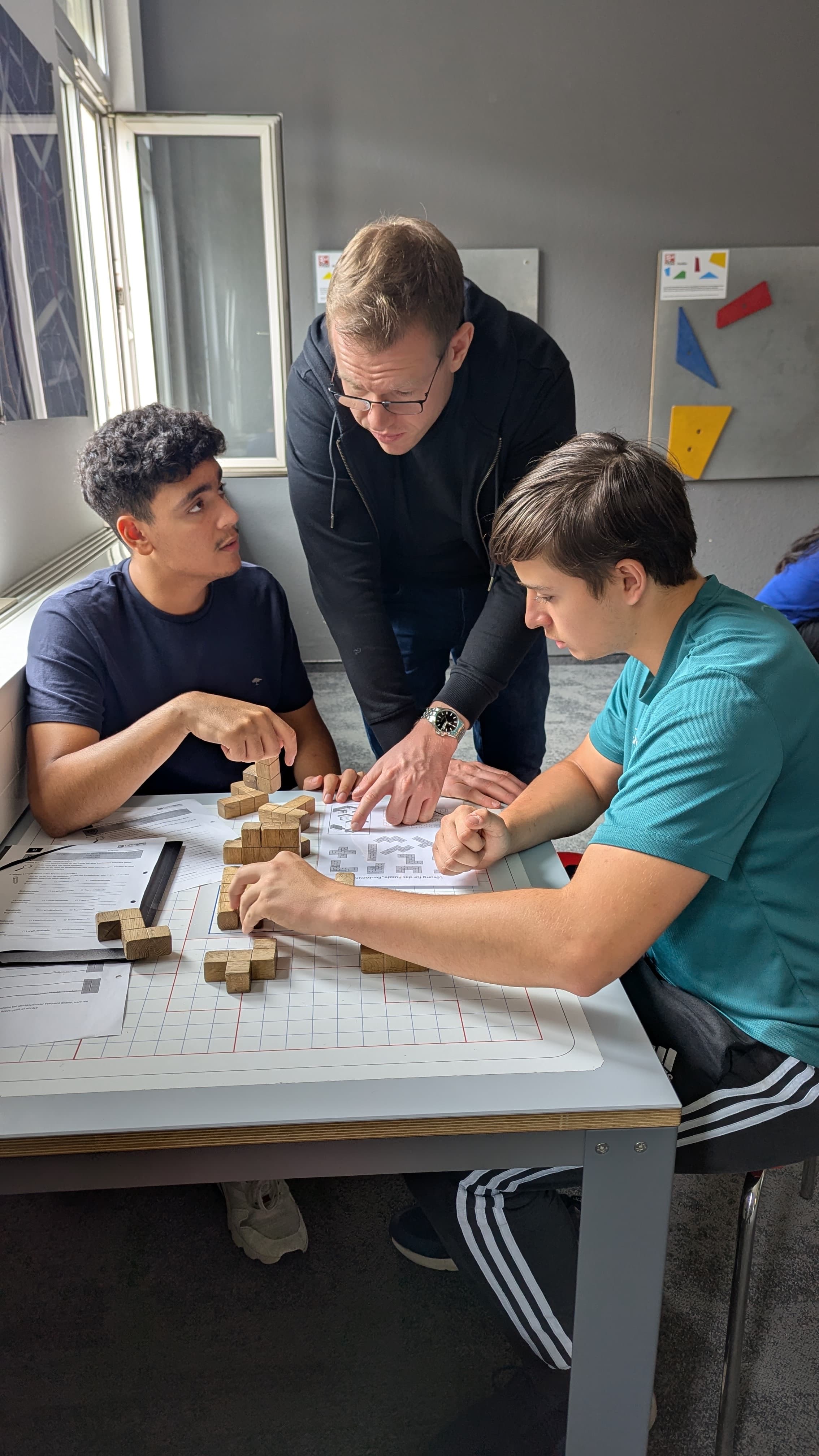 Lehrer und zwei Schüler arbeiten gemeinsam an einer Tüftelaufgabe mit Holzklötzen